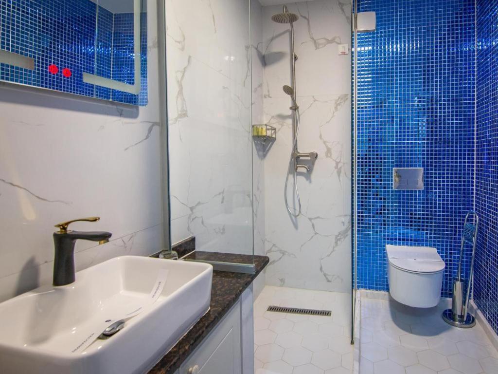 Walk-in shower with rain and handheld heads, blue mosaic accent wall, marble-look wall, wall-mounted toilet and sink at Hotel Lido by Phoenicia in Bucharest