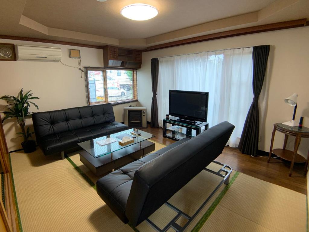 uma sala de estar com um sofá de couro preto e uma televisão em TY-Home em Asahikawa