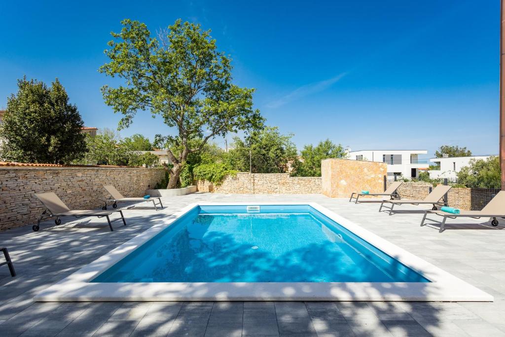 uma piscina com duas cadeiras e uma parede de tijolos em Apartments Cesare with Shared Pool em Ližnjan