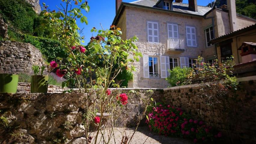 an old house with flowers in front of a stone wall at Au fil de l'eau in Cerdon