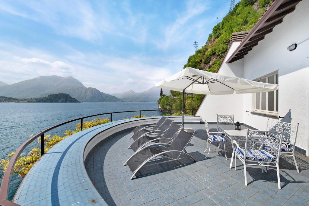 a patio with chairs and an umbrella next to the water at Villa Vittoria in Varenna