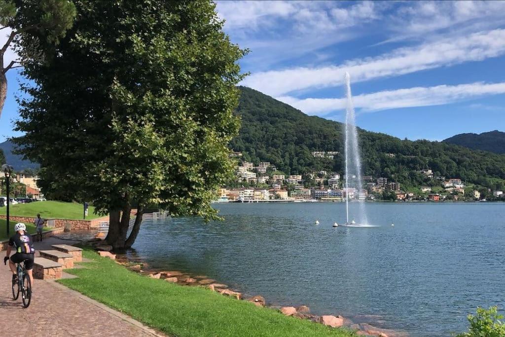 a person riding a bike next to a lake with a fountain at Tresa Bay House - Lugano Lake in Lavena Ponte Tresa