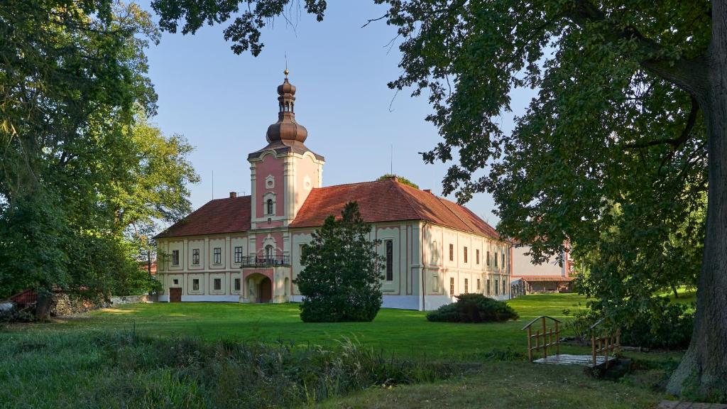 duży budynek z wieżą zegarową na zielonym polu w obiekcie Penzion Zámek Lešany w mieście Netvořice