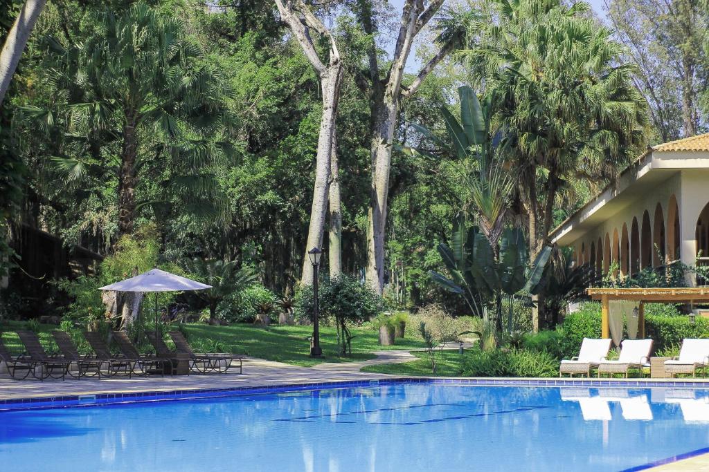 a swimming pool with chairs and an umbrella and trees at Hotel Resort e Golfe Clube dos 500 in Guaratinguetá