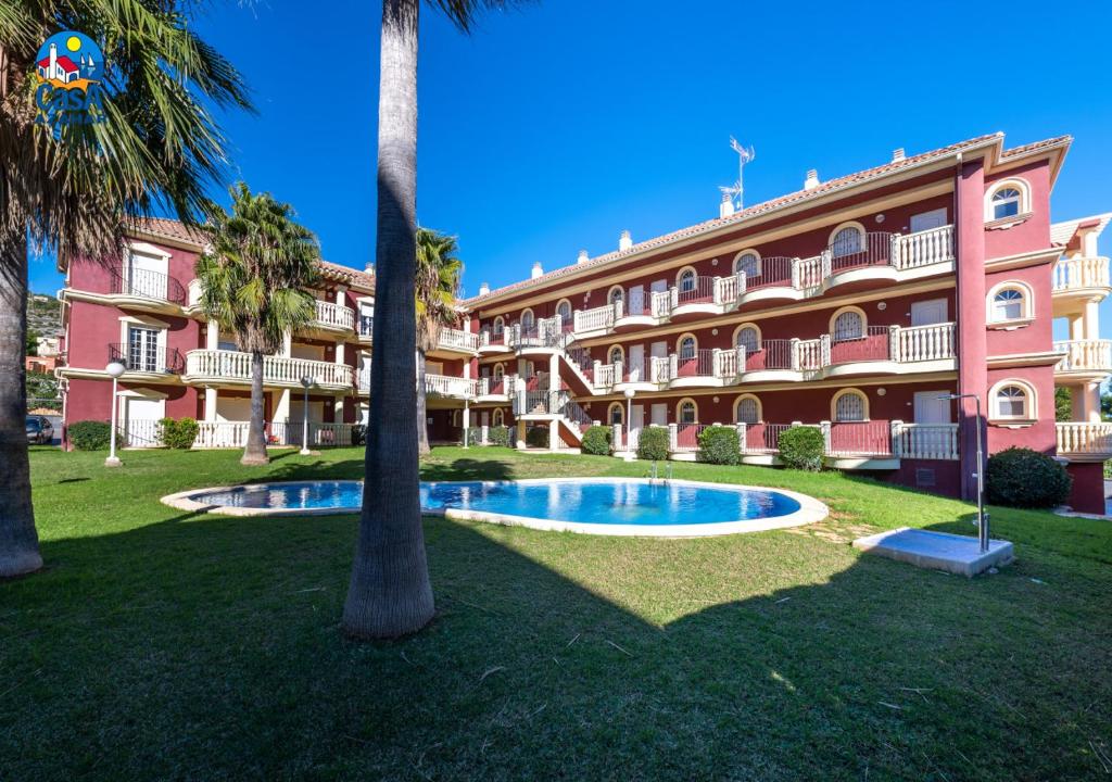 a large pink building with a palm tree and a swimming pool at Apartamentos Madeira Casa Azahar in Alcossebre
