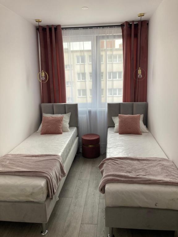 two beds in a room with red curtains and a window at Apartament 80’s in Kołobrzeg