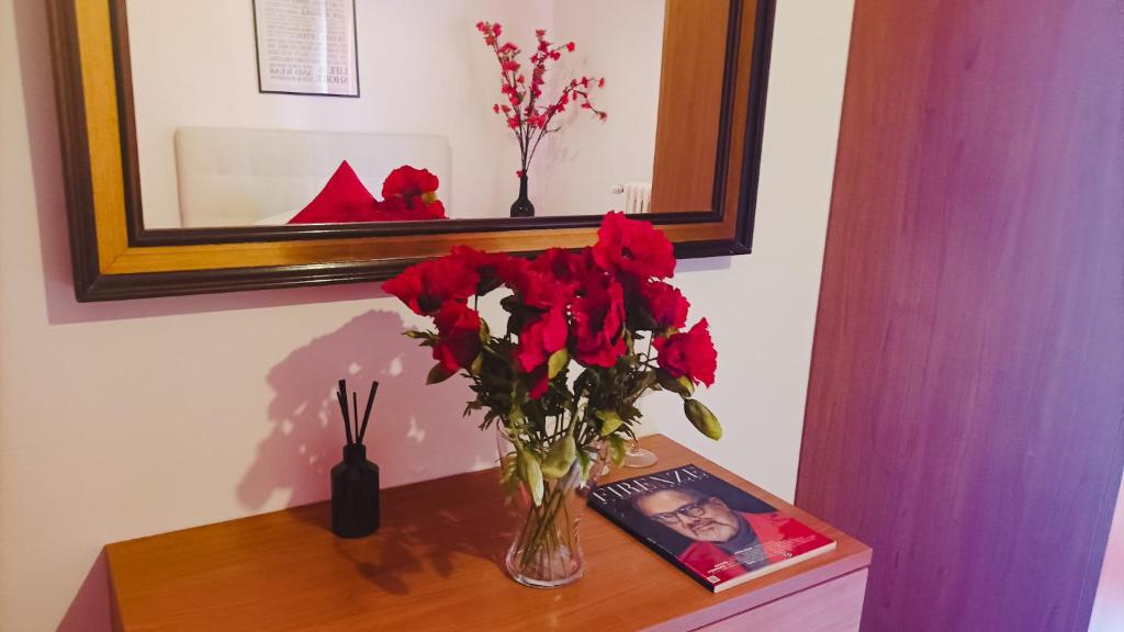 a vase of red flowers on a table with a mirror at Unique & beautiful bedroom in central of Florence in Florence