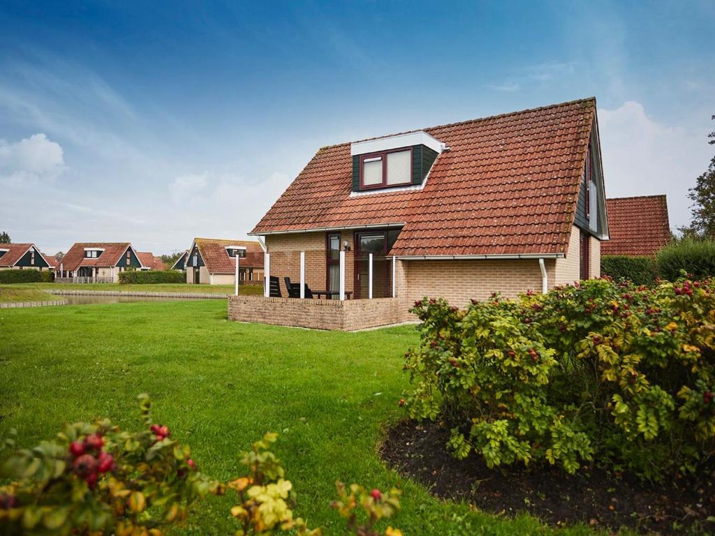 una casa con techo rojo en un patio verde en Cozy holiday home with two bathrooms, in Zeeland, en Heinkensand
