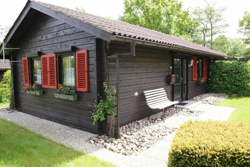 a black cabin with red shuttered windows and a bench at Blockhaus mit W LAN sehr strandnah in Damp
