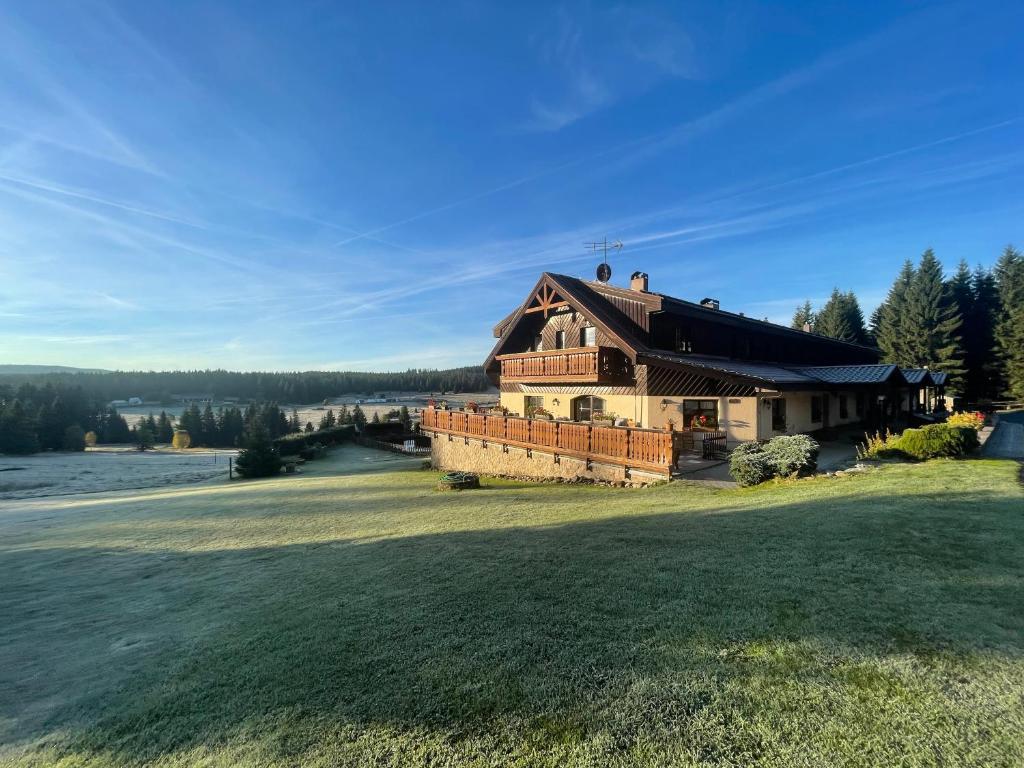 a large house on a grassy field next to a lake at Pension Hones in Horská Kvilda