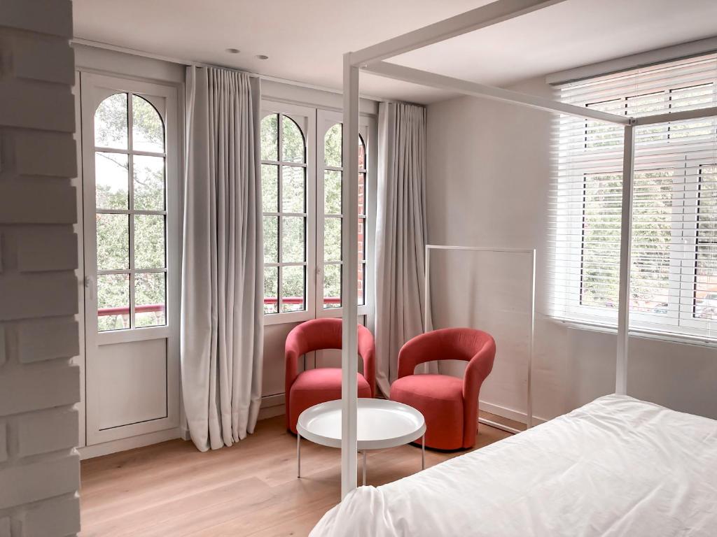 a bedroom with two red chairs and a bed and windows at Doux Foyer in De Haan