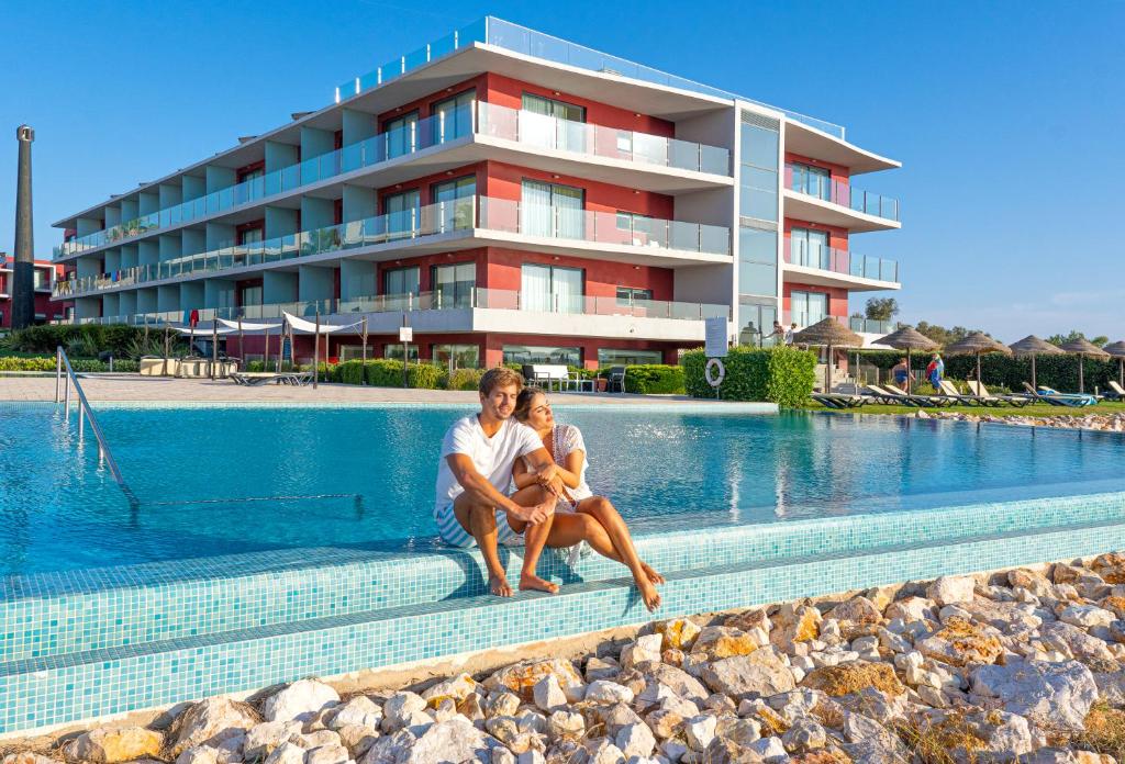 un homme et une femme assis à côté d'une piscine dans l'établissement Agua Hotels Riverside, à Ferragudo