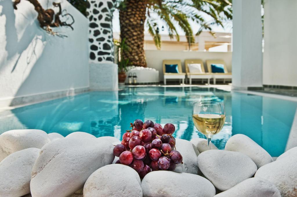 a glass of wine and a bowl of grapes next to a swimming pool at Galatia Villas in Fira