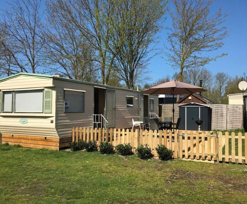 a small caravan with a fence and an umbrella at Chalet K2 op de Holle Poarte te Makkum in Makkum