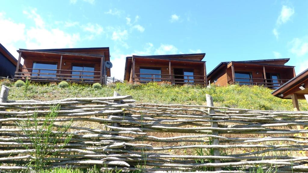 two houses on a hill with a wooden fence at Hotel y Cabañas Terrazas Vista al Mar hct in Ancud