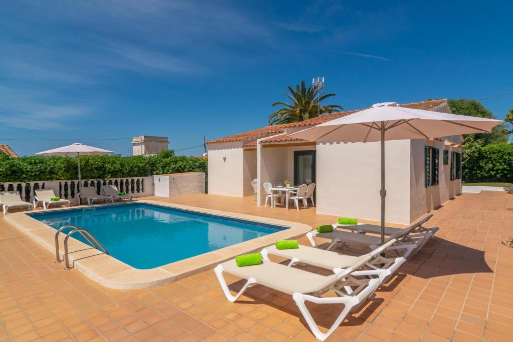 una piscina con dos tumbonas y una sombrilla en Villa Marina -Cala EnPorter-, en Cala'n Porter