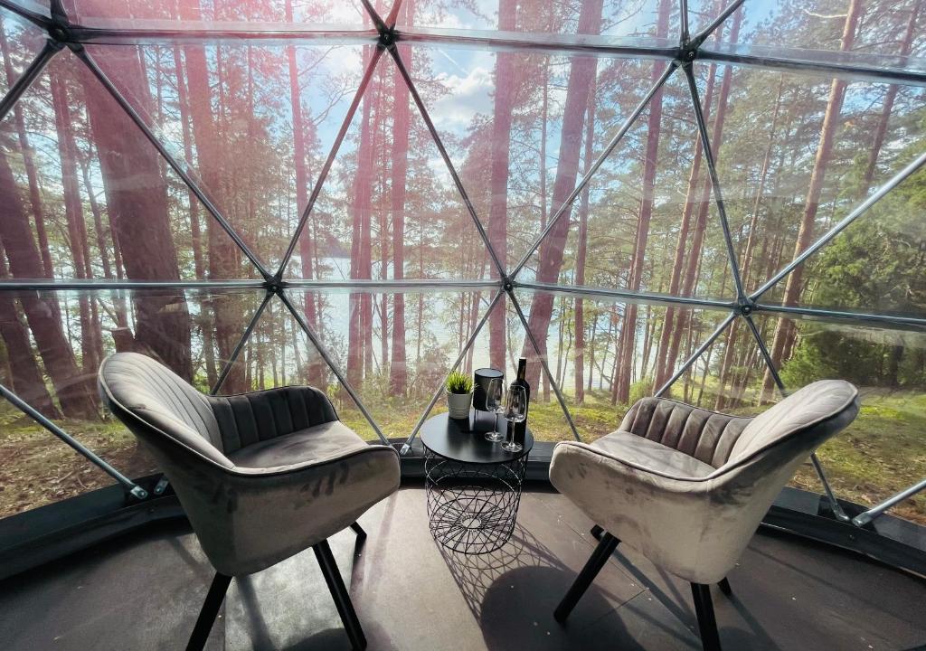 dos sillas y una mesa frente a una casa de cristal en Skywoods.glamping en Molėtai