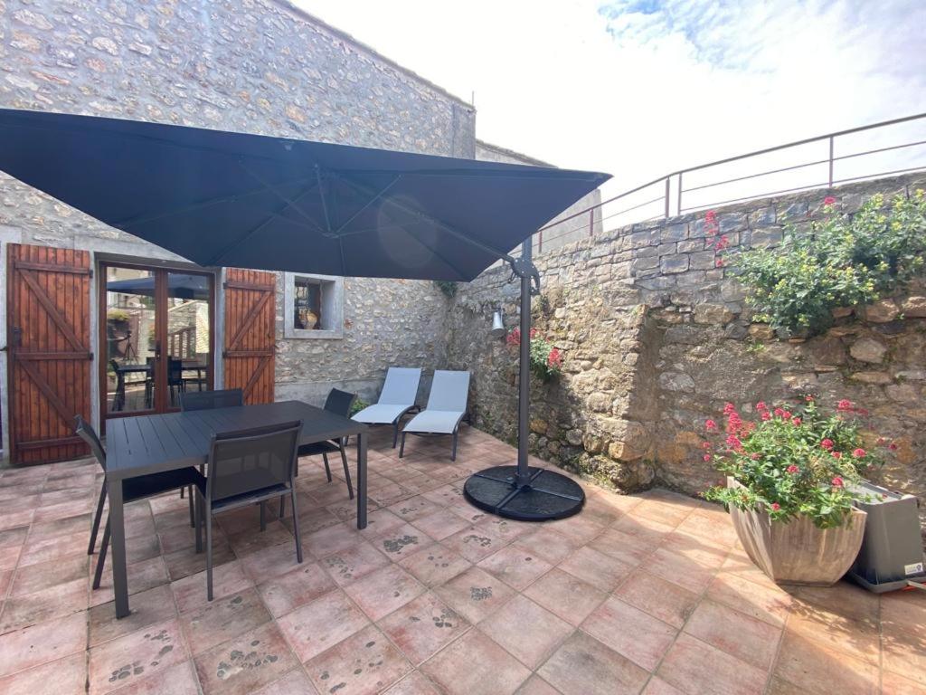 een patio met een tafel en stoelen en een parasol bij La Maison Des Vendangeurs in Villesèque-des-Corbières