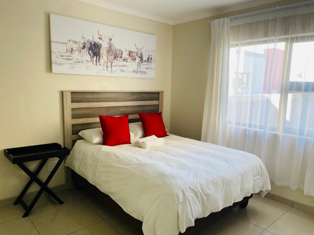 Schlafzimmer mit einem Bett mit roten Kissen und einem Fenster in der Unterkunft E & P Cave in Swakopmund