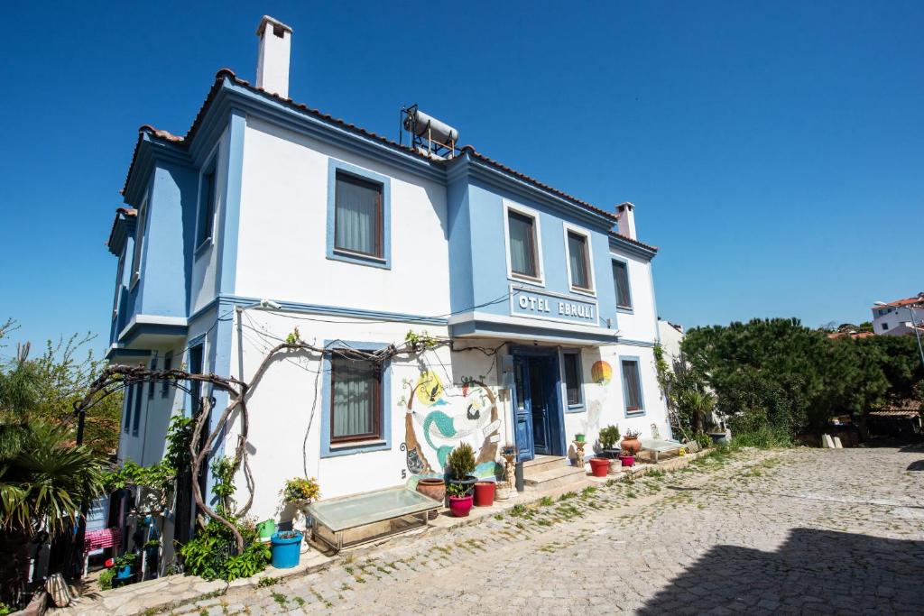 ein weißes Haus mit blauem Trimm auf einer Kopfsteinpflasterstraße in der Unterkunft Ebruli Hotel in Bozcaada