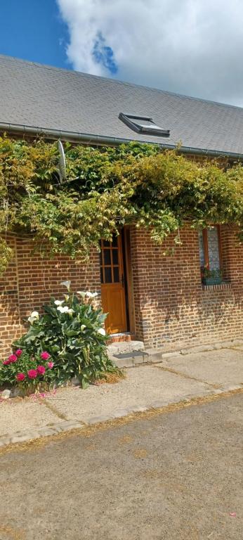 a brick building with a brown door and flowers at logement dans ferme equestre in Lyons-la-Forêt