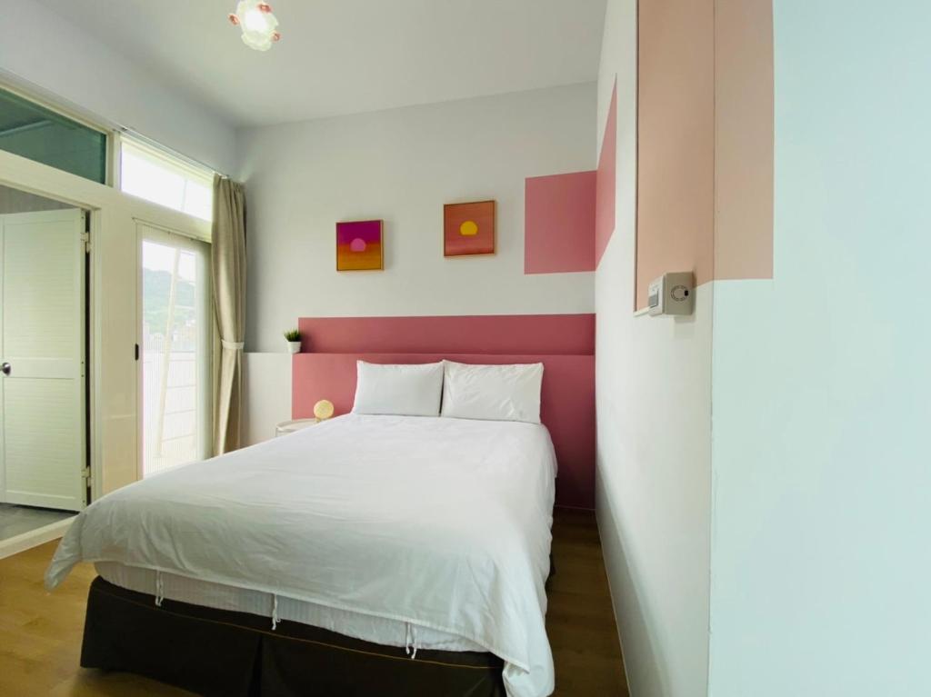 a bedroom with a white bed with a pink headboard at 小逗民宿 in Taitung City