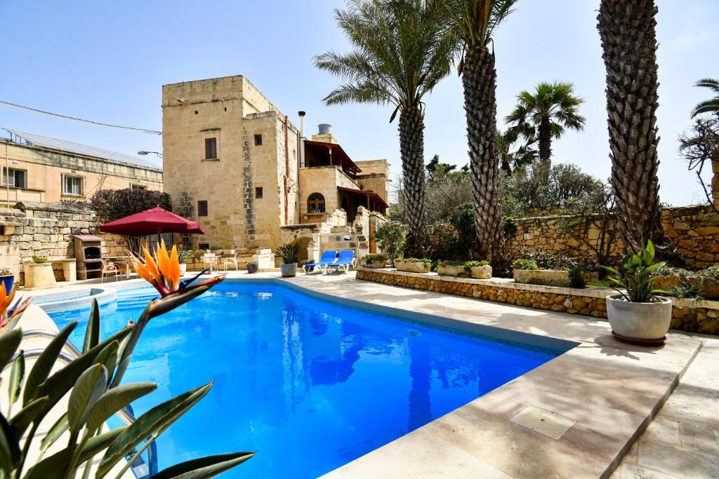 a swimming pool in front of a house with palm trees at Maria's B&B in Għasri