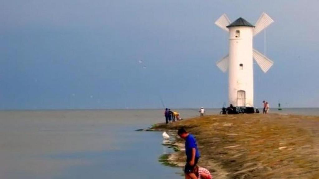 a man standing in the water in front of a lighthouse at POD BLUSZCZEM in Świnoujście