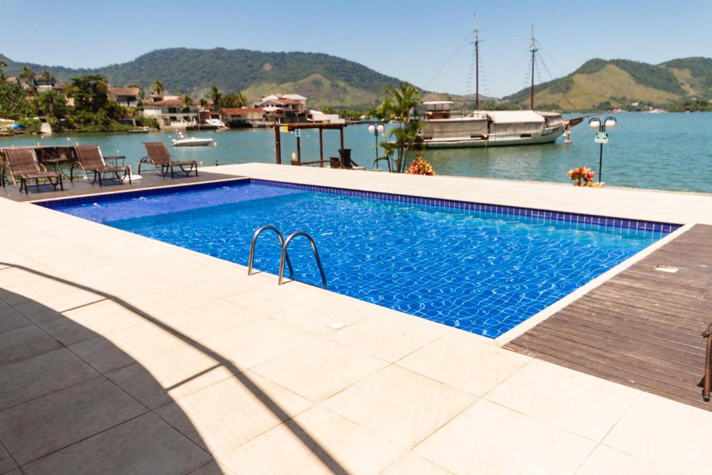 a swimming pool next to the water with a boat at Sua casa fora de casa! in Angra dos Reis