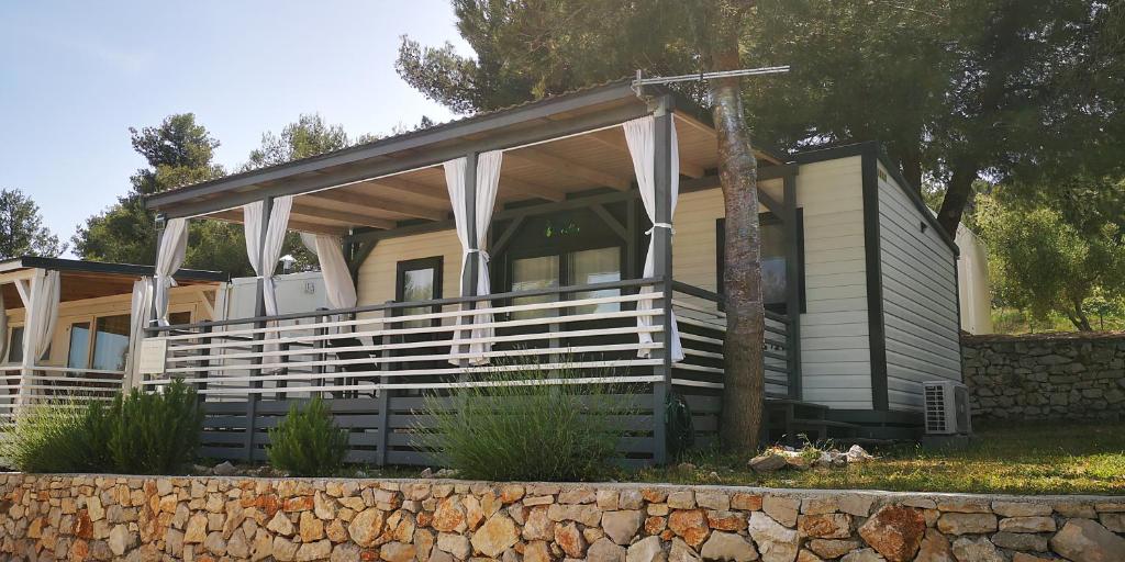 a house with a porch and a stone wall at Mobile home Lux otok Murter in Jezera