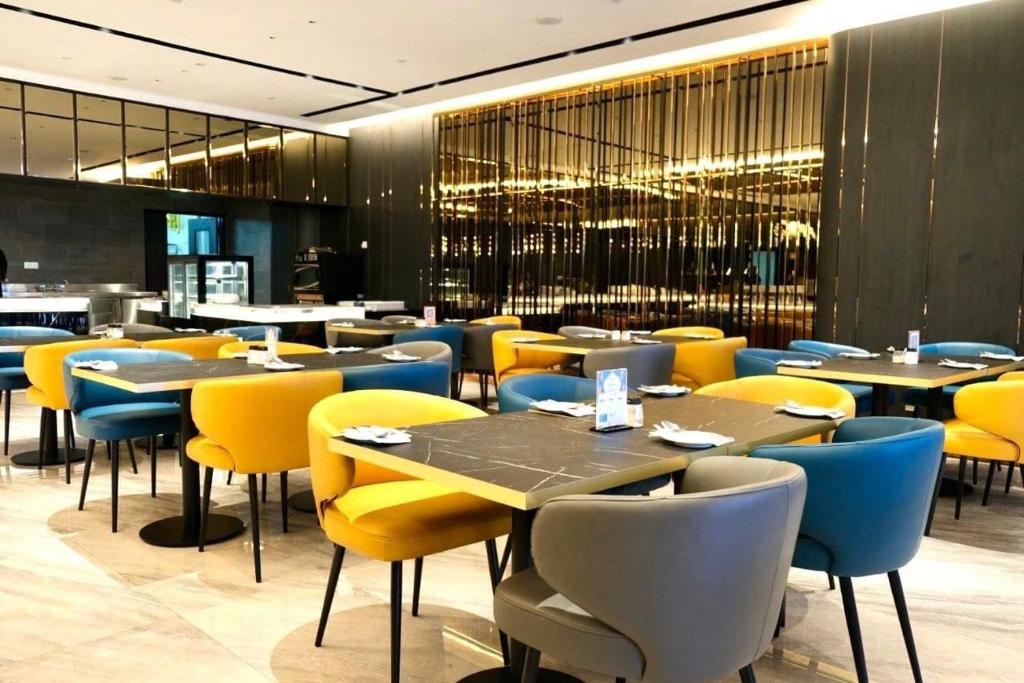 A modern hotel dining room with yellow and blue upholstered chairs, dark tables, and buffet equipment.