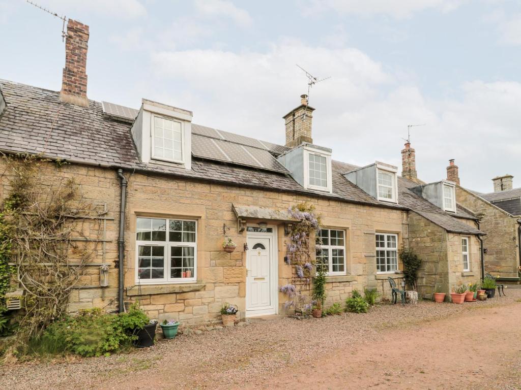 una antigua casa de piedra con una puerta y ventanas blancas en 5 Swinton Mill Farm Cottage, en Coldstream