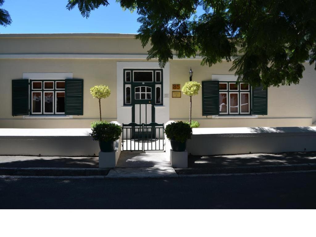 ein weißes Haus mit schwarzen Fensterläden und Pflanzen in der Unterkunft Cypress Cottage in Graaff-Reinet