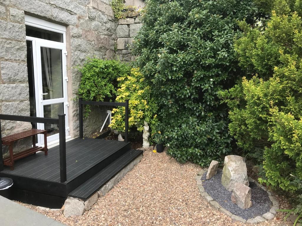 un banc en bois à côté d'un bâtiment avec un bush dans l'établissement Craignair Cottage, à Dalbeattie