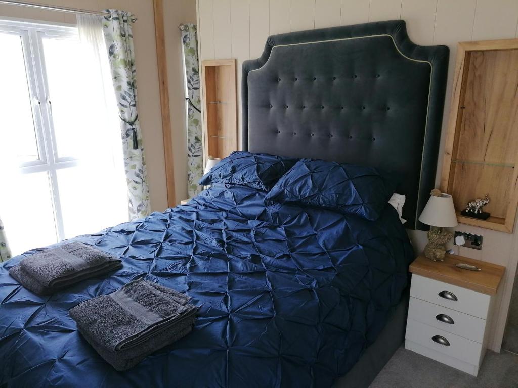 a large bed with a blue comforter and a window at STUNNING, PEACEFUL LODGE on edge of New Forest and 800m from sea ENTERTAINMENT and LEISURE PASSES INCLUDED in Milford on Sea