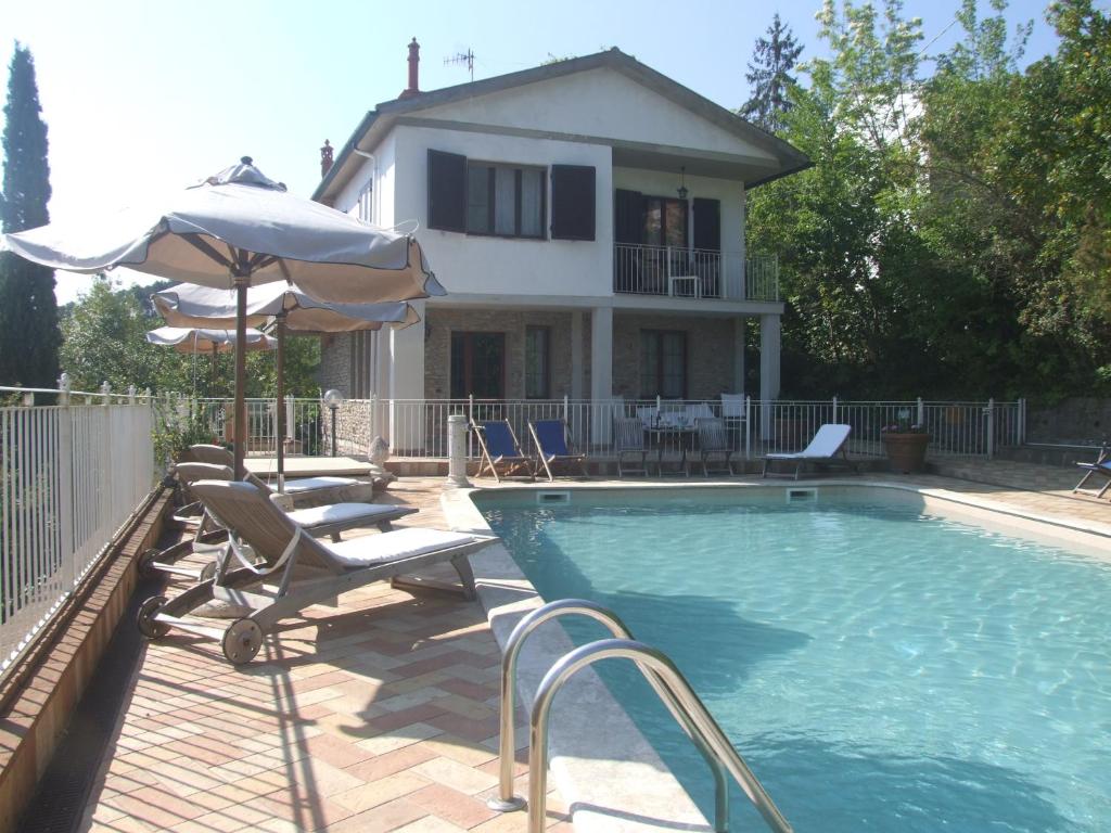 a swimming pool with chairs and an umbrella and a house at Vacanze Toscane In The Country in Sassetta