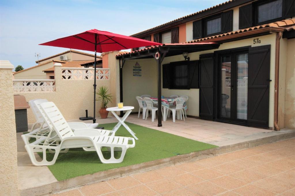 une terrasse avec des chaises blanches, une table et un parasol dans l'établissement Belle villa de vacances climatisée, residence TAMARIS, wifi, 2 chambres 4 à 6 couchages, accès payant pour les piscines et animations , PORTIRAGNES PLAGE LRTAMA57, à Portiragnes
