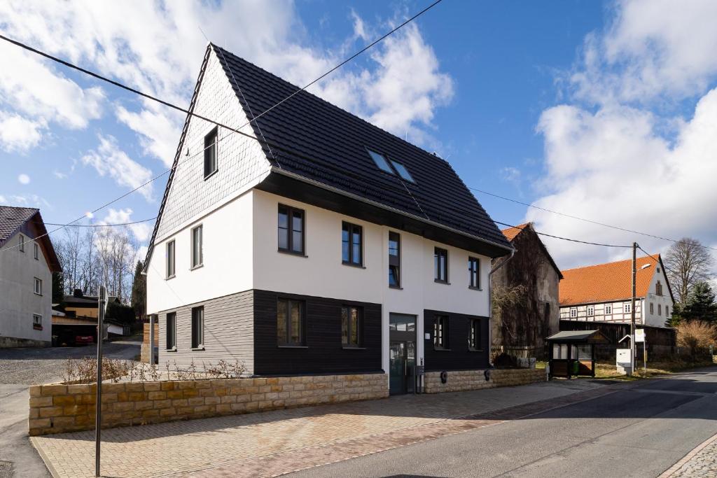 a white house with a black roof on a street at Neues Ferienhaus in Kurort Gohrisch