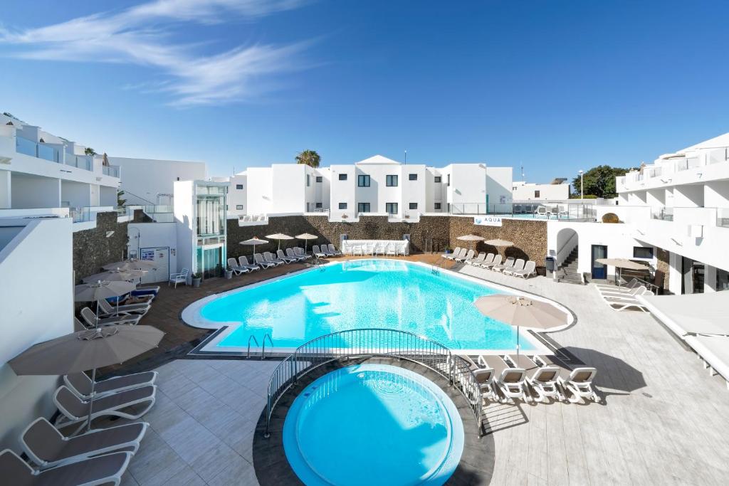 una gran piscina con sillas y sombrillas en un edificio en Aqua Suites en Puerto del Carmen