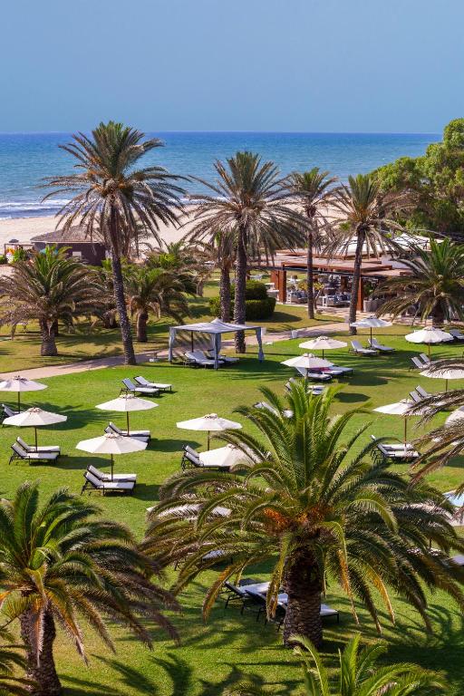 a beach with palm trees and chairs and umbrellas at OCEANA Hotel & Spa in Hammamet