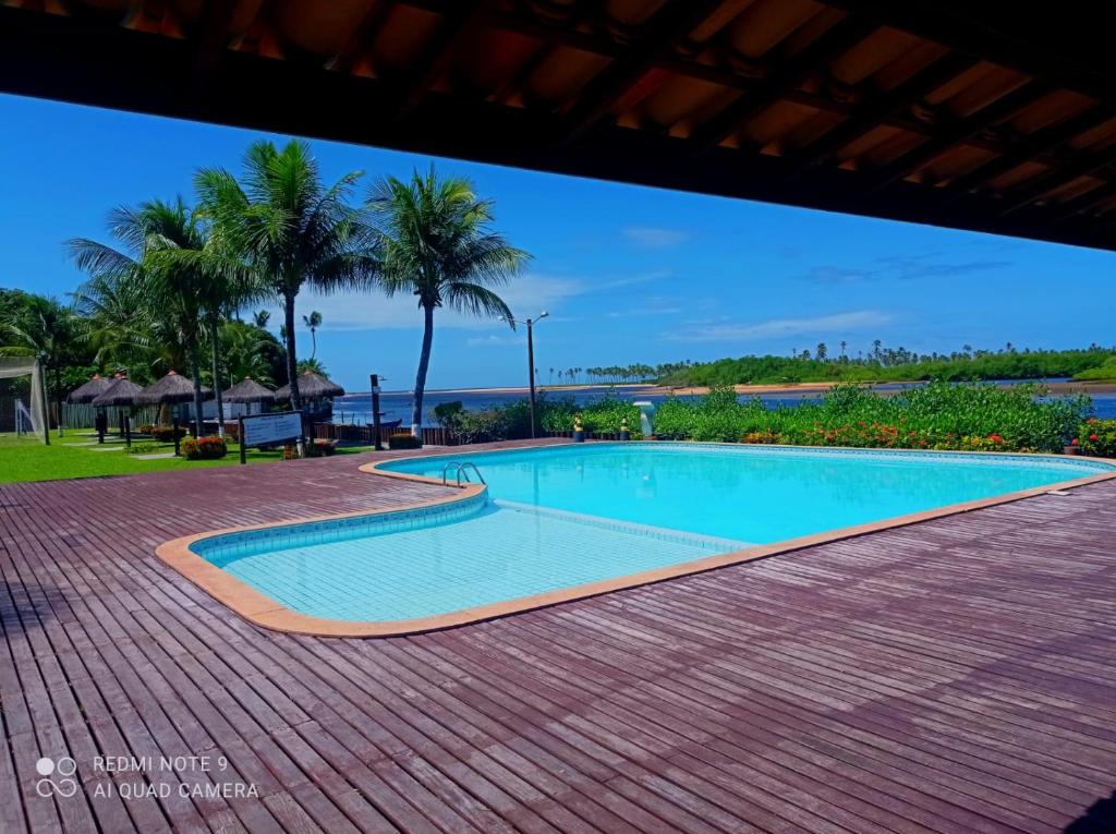 a swimming pool with palm trees and the ocean at Pier Jacuípe Residencial in Camaçari