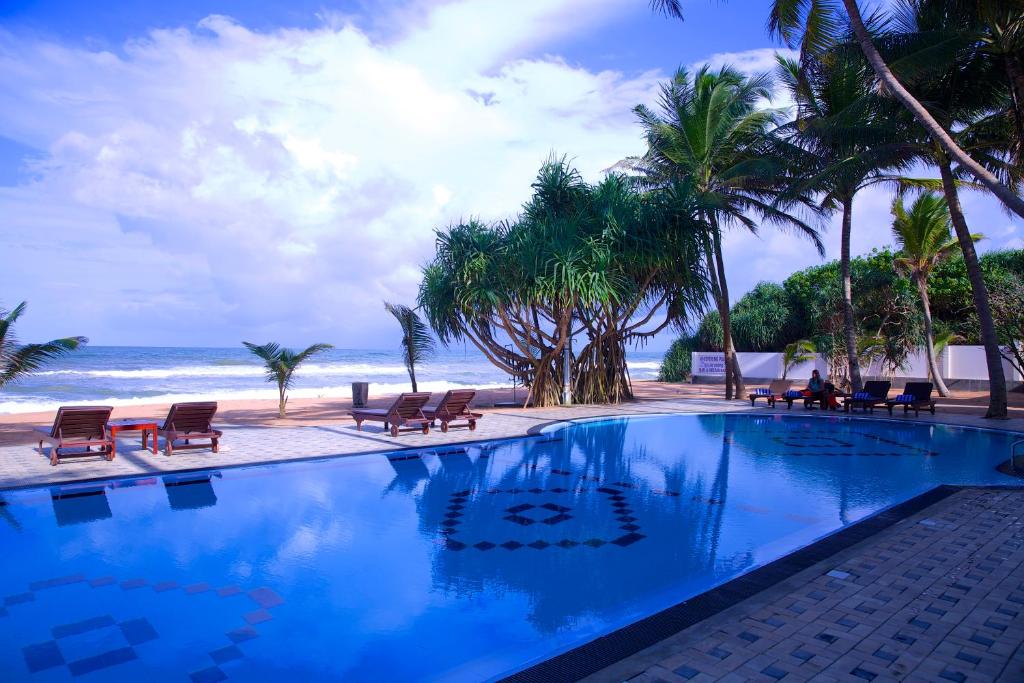 einen Pool neben einem Strand mit Palmen in der Unterkunft Whispering Palms Hotel in Bentota