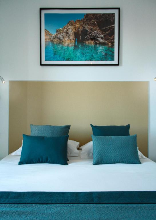 a bed with blue pillows and a picture on the wall at Hotel l'Isolella in Porticcio