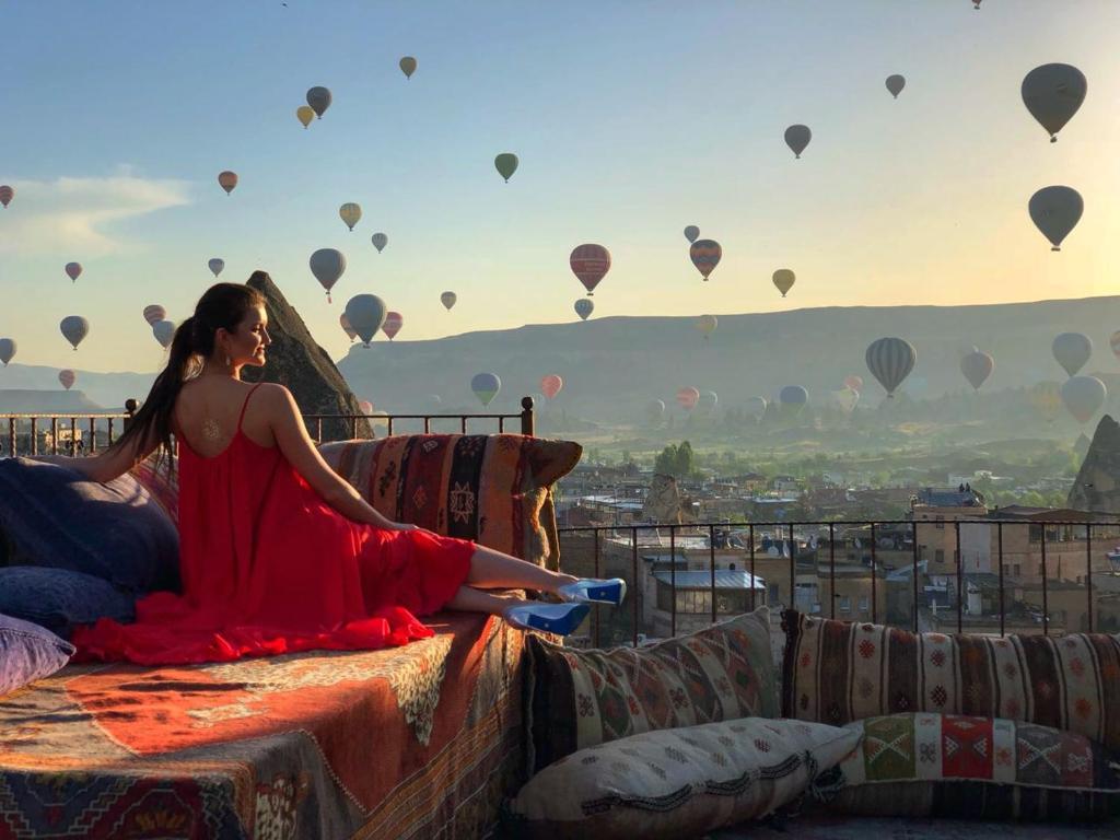 una donna seduta su un letto con mongolfiere di Vista Cave Hotel a Göreme