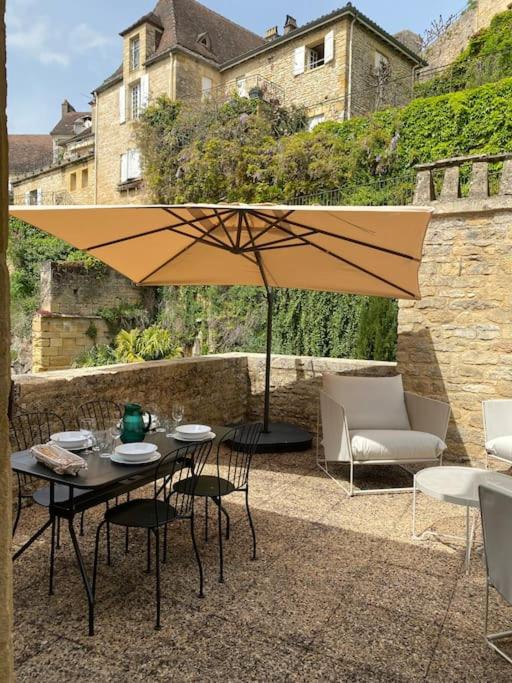 un patio avec une table, des chaises et un parasol dans l'établissement Les Courtines - Appartement de caractère à la Roque-Gageac - Les Lauriers, à La Roque-Gageac