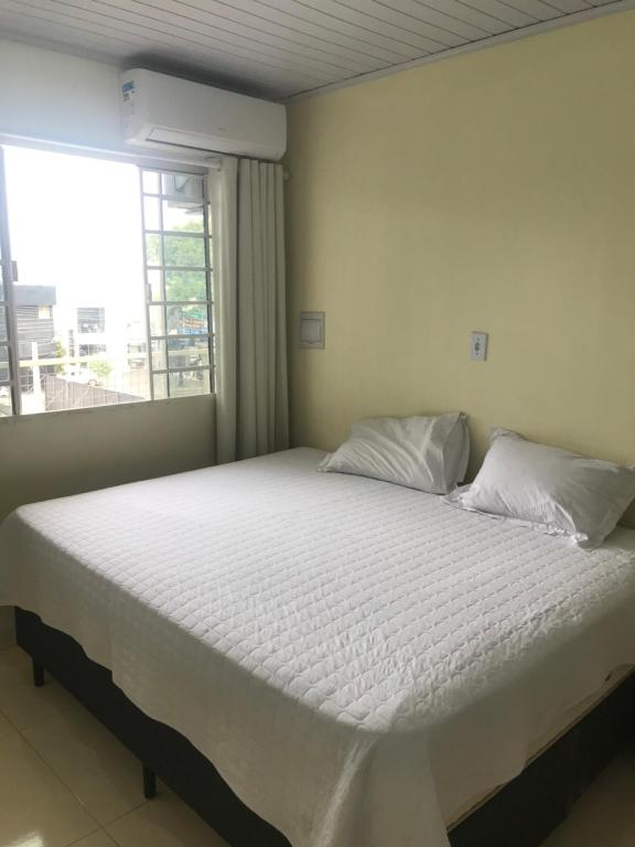 um quarto com uma cama branca e uma janela em Loft confortável no Centro em Chapecó