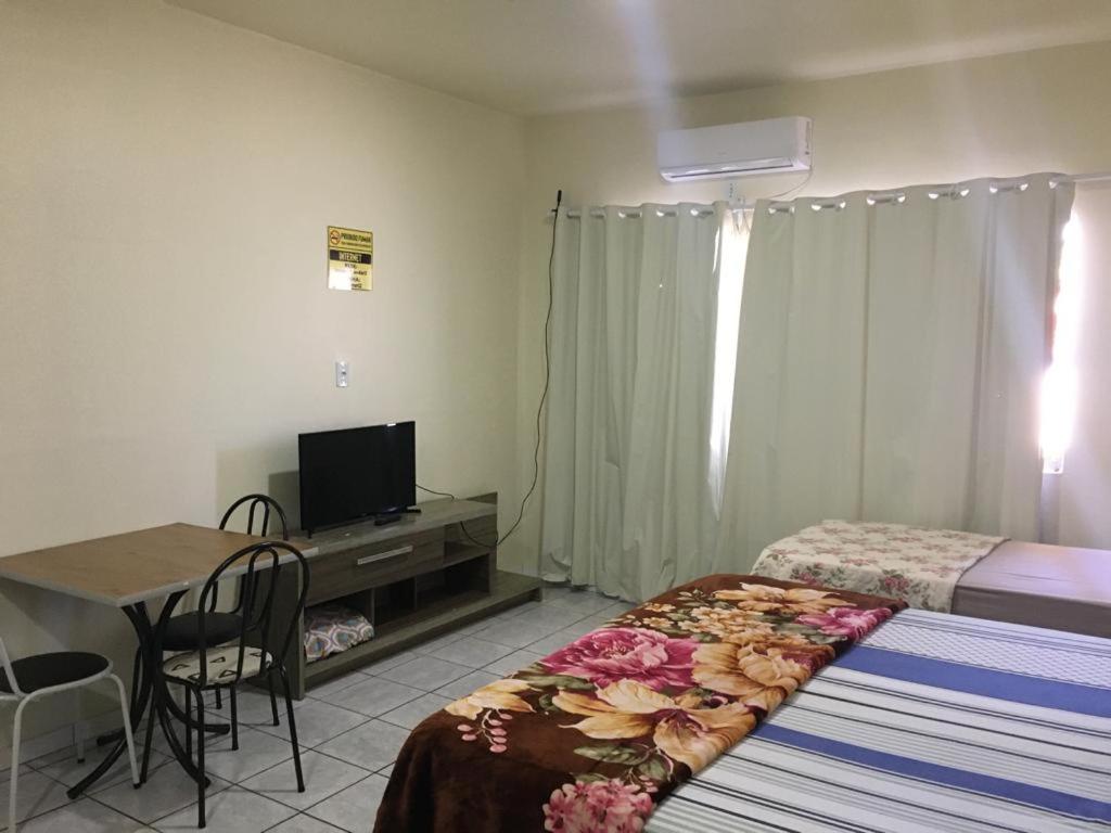 a bedroom with a bed and a desk with a television at Flat no centro in Chapecó