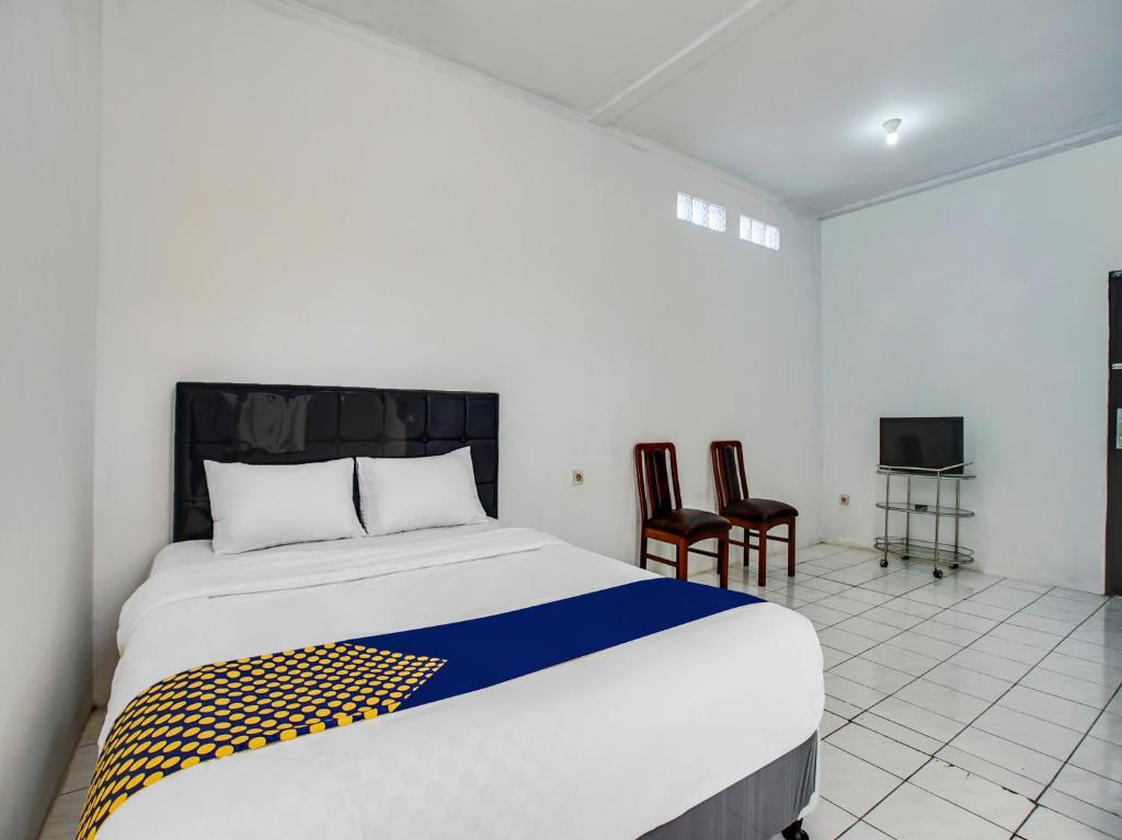 Cette chambre comprend un lit avec deux chaises et une télévision. dans l'établissement SPOT ON 91117 Sriwijaya Residence Syariah, à Bandung