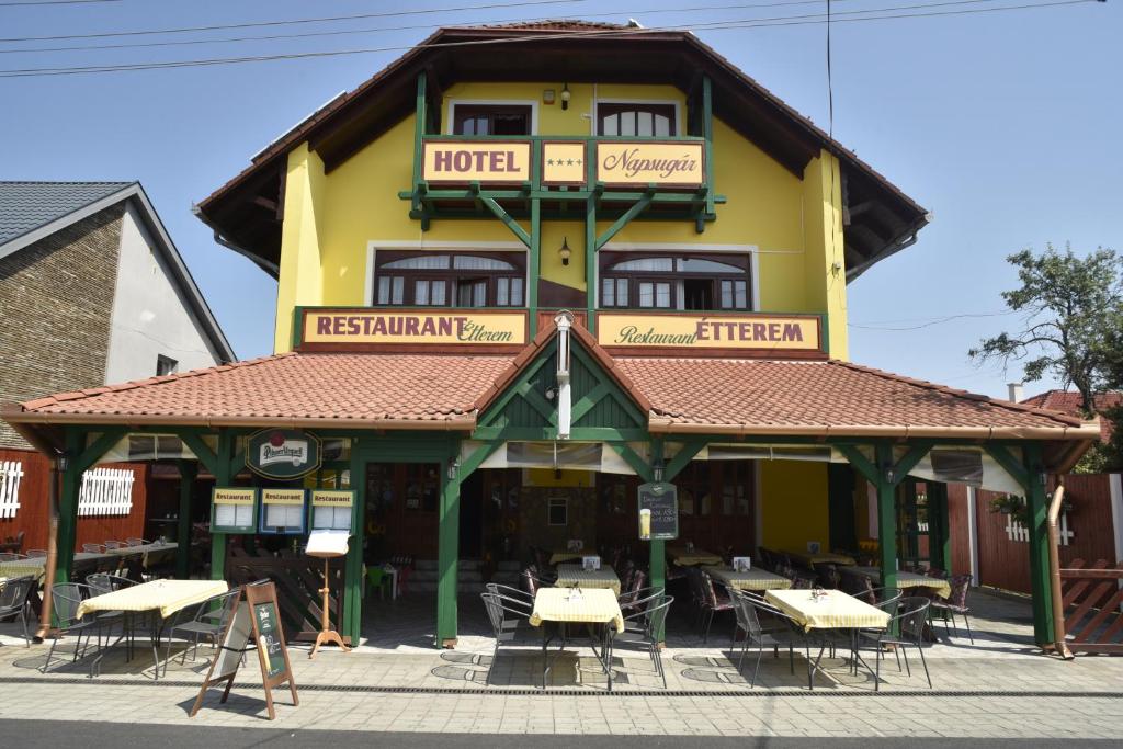 un bâtiment avec des tables et des chaises devant lui dans l'établissement Hotel Napsugár, à Balatonmáriafürdő