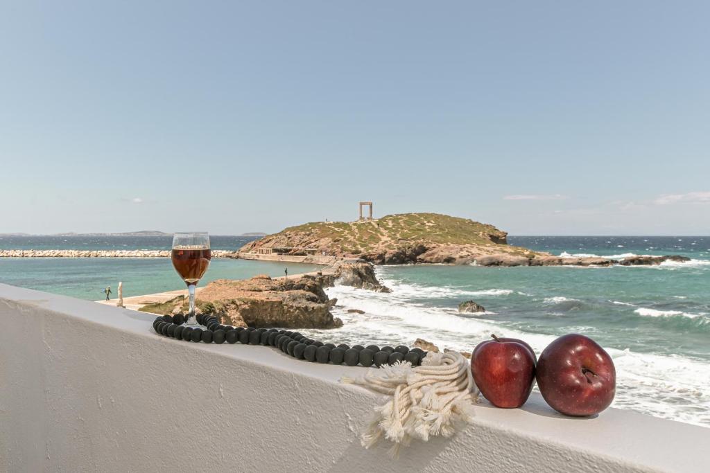 una copa de vino y dos manzanas en una cornisa cerca del océano en Flèria Seaview Suites, en Naxos Chora